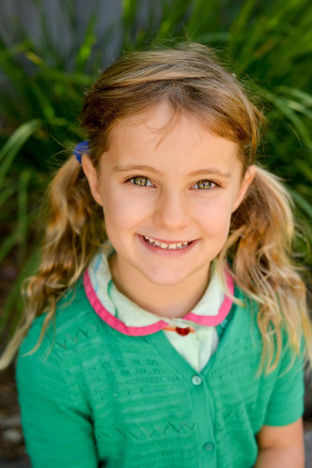 A smiling student in a green cardigan, photographed outdoors